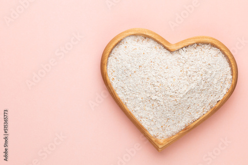 Wheat flour in a wooden heart shape bowl on a pastel background.