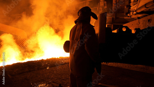 Metallurgist worker in protective uniform at the steel plant controlling hot molten metal pouring process. Man working in heavy industry.