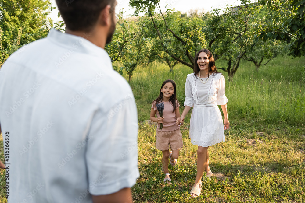 blurred man near happy wife and daughter holding hands near green trees. blurred man near happy wife and daughter holding hands near green trees.