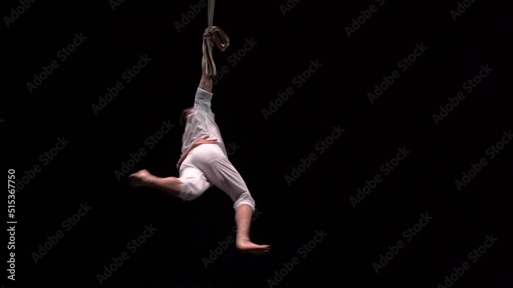 Muscular circus aerialist on the aerial straps in black studio Muscular circus aerialist on the aerial straps in black studio