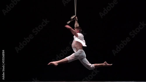 Muscular white circus artist on the aerial straps on black background in slowmotion. Concept of individuality, creativity and self-confidence photo