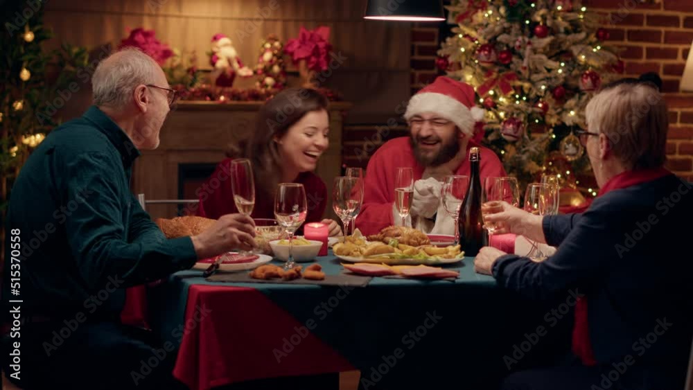 Festive family talking with man disguised as Santa Claus while drinking champagne at Christmas dinner. Happy people celebrating winter holiday tgether while enjoying home cooked food. Tripod shot Festive family talking with man disguised as Santa Claus while drinking champagne at Christmas dinner. Happy people celebrating winter holiday tgether while enjoying home cooked food. Tripod shot