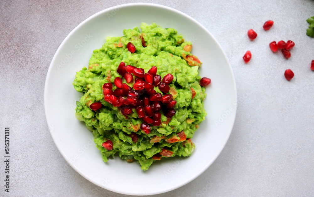 green pea guacamole with pomegranate seeds on a white plate of selective focus. green pea guacamole with pomegranate seeds on a white plate of selective focus.