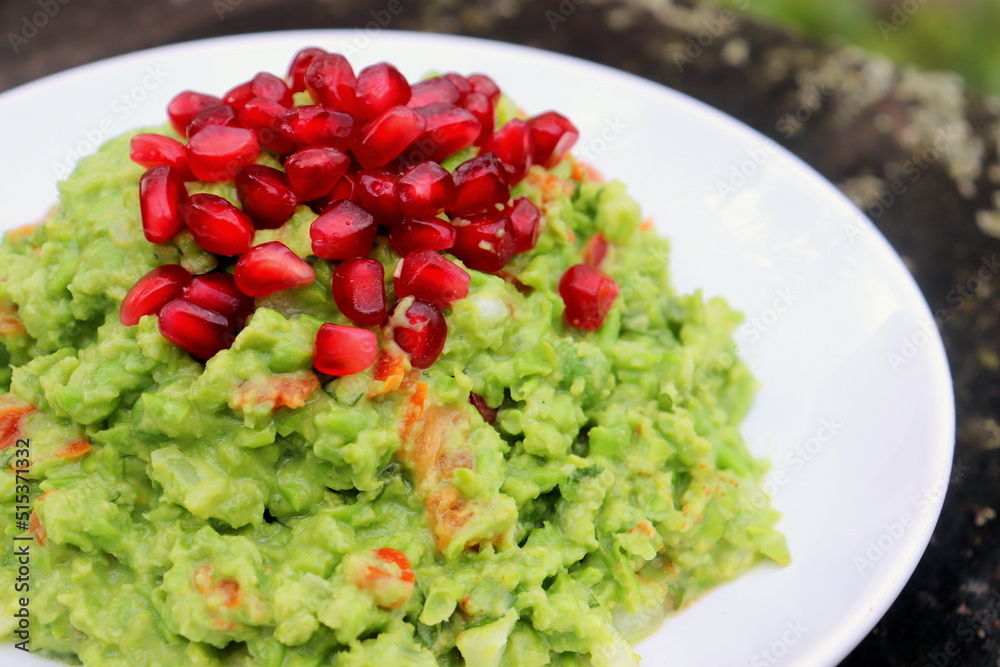 green pea guacamole with pomegranate seeds on a white plate of selective focus.
