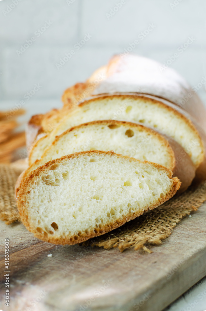 Slices of fresh baked bread on a wooden cutting board on a light background. Rustic style. The concept of homemade bread. Vertical orientation. Slices of fresh baked bread on a wooden cutting board on a light background. Rustic style. The concept of homemade bread. Vertical orientation.