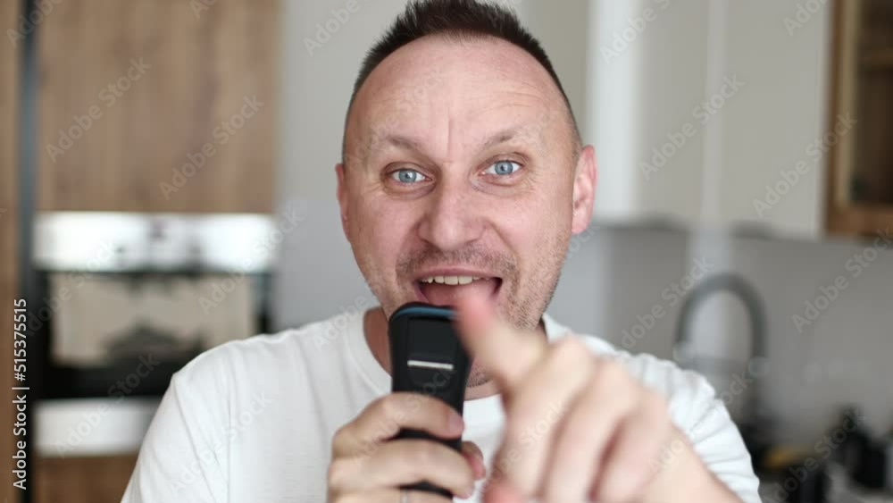 Cheerful funny handsome caucasian man guy in white t shirt shaving singing song into razor having fun shaving in kitchen at home dancing music humorous hygiene. having fun. everyday life. Cheerful funny handsome caucasian man guy in white t shirt shaving singing song into razor having fun shaving in kitchen at home dancing music humorous hygiene. having fun. everyday life.