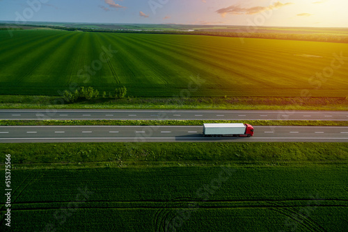 red cargo truck on the highway. asphalt road among green fields at sunset. cargo delivery and transportation concept