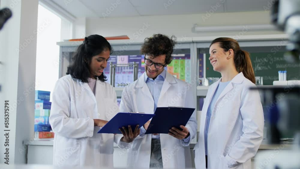 science research, work and people concept - international group of happy scientists with clipboards discussing report in laboratory