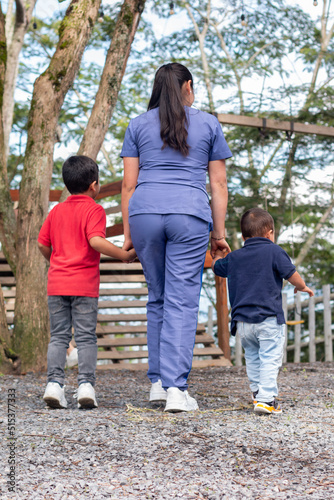 A doctor holds hands with two children for an occupational therapy session at a playground.