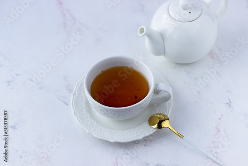 A white cup of tea and a white teapot on a marble table