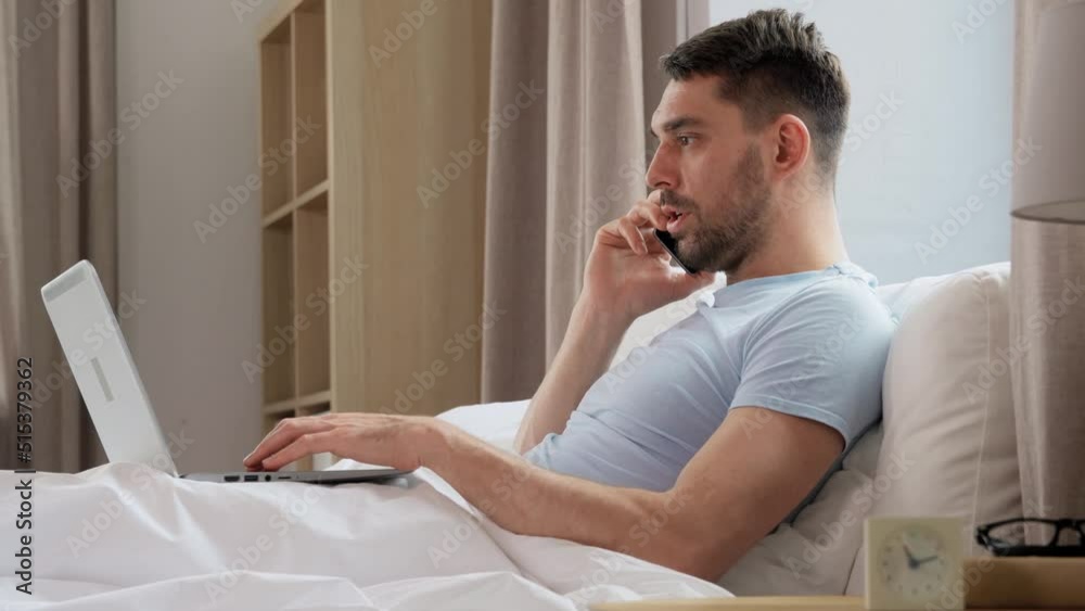 people, technology and remote job concept - man with folder and laptop computer calling on smartphone in bed at home bedroom people, technology and remote job concept - man with folder and laptop computer calling on smartphone in bed at home bedroom
