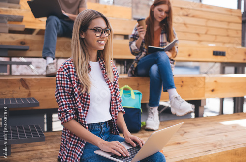 Group of diverse students sitting outdoors at university campus with laptop computers and books. Three friends learning and preparing homework for school lessons. Female keyboarding request on web