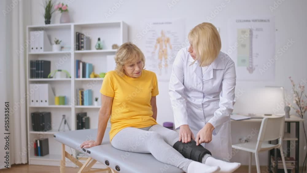 Medical worker putting support band on senior patient's leg, rehabilitation care Medical worker putting support band on senior patient's leg, rehabilitation care