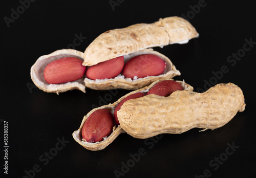 A beautiful young split peanuts in a shell with bright beautiful nuts inside and a small split peanut next to it on a glossy black background with reflection. Close-up