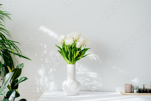 Photo Scandinavian home interior with spring bouquet of white tulip flowers in ceramic vase standing on cabinet