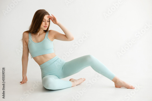 Beautiful athletic girl in a blue fitness suit sits on a white background