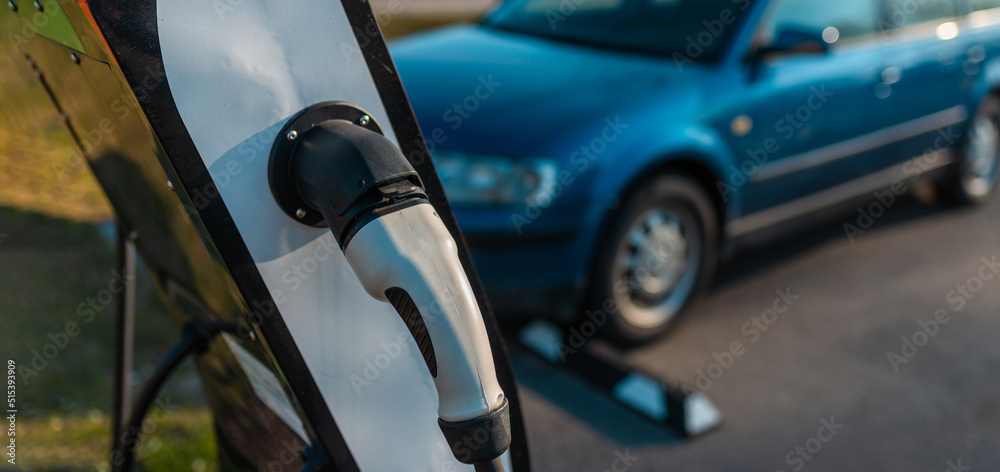 Banner image. power cord for electric car. Green station.Power supply for electric car battery charging.Blurred car in the background.Selective focus.Closeup.