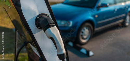 Banner image. power cord for electric car. Green station.Power supply for electric car battery charging.Blurred car in the background.Selective focus.Closeup.