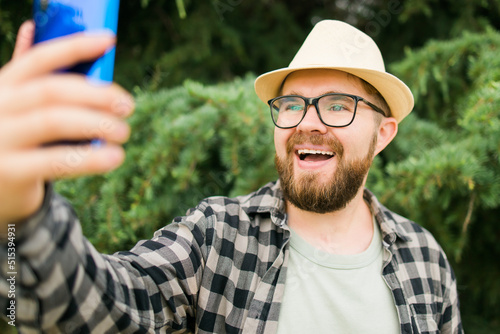 Man taking selfie portrait over tree background - Happy millennial guy enjoying summer holidays in city - Youth and technologies © satura_