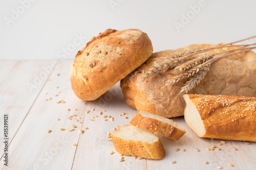 Fresh white wheat bread, round classic, ciabatta, french baguette, wheat ears and grains on white wooden background. Bread making, bakery, healthy food. Bread background. Light mockup