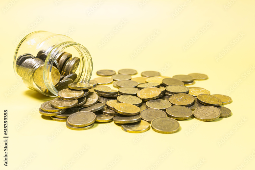 An overturned glass jar against the background of a scattering of yellow coins close-up. An overturned glass jar against the background of a scattering of yellow coins close-up.