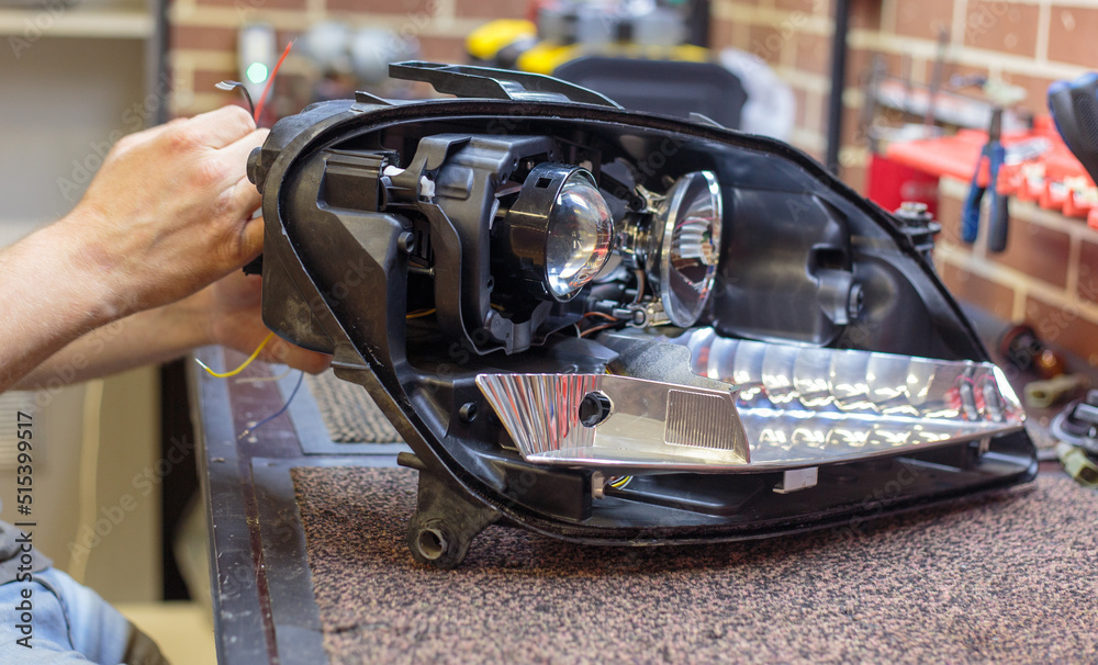 Car headlight in repair close-up. The car mechanic installs the lens in the headlight housing. The concept of a car service.Installation of LED lenses in the headlight. LED lens.Restoration of optics. Car headlight in repair close-up. The car mechanic installs the lens in the headlight housing. The concept of a car service.Installation of LED lenses in the headlight. LED lens.Restoration of optics.