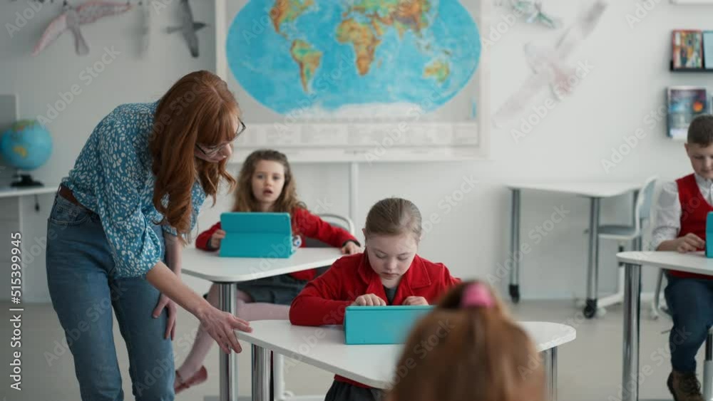 Teacher walking through class and watching children using digital tablets during lesson at primary school.