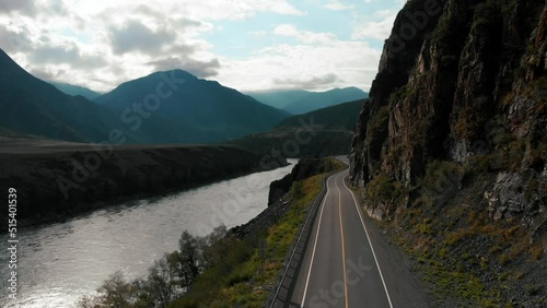Aerial cloudy day view automobile road near river surrounded cliff altay mountains. natural mountain valley blue sky sun light calm water surface. High quality FullHD footage