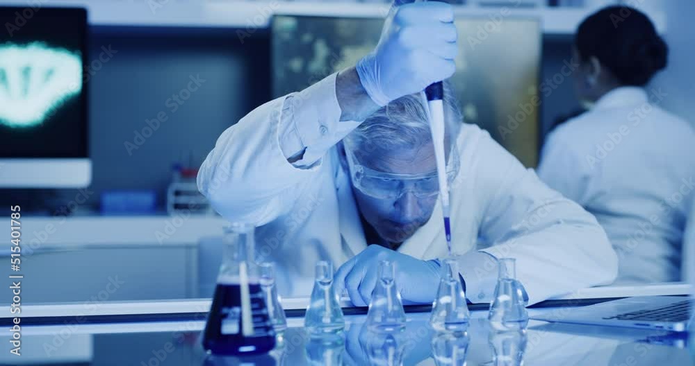 Mature laboratory scientist testing phenolphthalein chemical reaction with a beaker and pipette in ultraviolet lit lab. Serious doctor wearing protective glasses, experimenting alkaline presence test Mature laboratory scientist testing phenolphthalein chemical reaction with a beaker and pipette in ultraviolet lit lab. Serious doctor wearing protective glasses, experimenting alkaline presence test