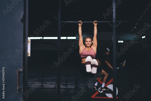 Strong female bodybuilder doing pull-ups for training biceps during workout exercising, portrait of Caucasian woman keeping athletic body shape in tonus have energetic warm up at horizontal bars © BullRun