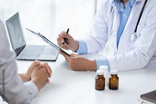Doctor and patient sitting and talking at medical examination at hospital office  close-up. Therapist filling up medication history records. Medicine and healthcare concept.