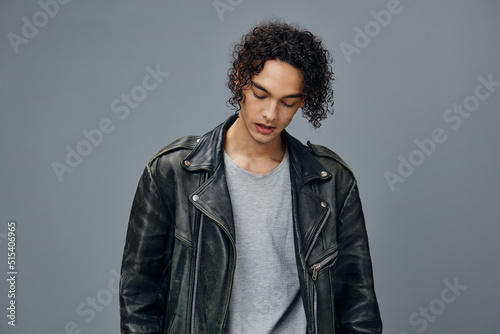 Serious adorable stylish tanned curly man leather jacket looks aside posing isolated on over gray studio background. Cool fashion offer. Huge Seasonal Sale New Collection concept. Copy space for ad