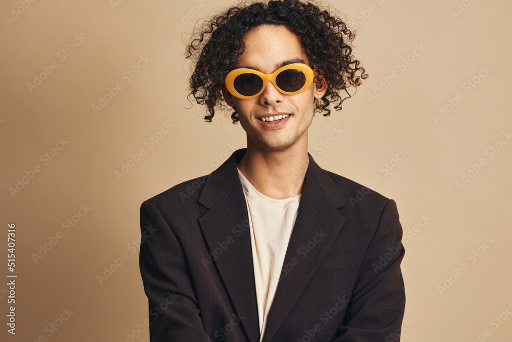 Fototapeta premium Closeup portrait of awesome tanned curly man in classic brown jacket trendy sunglasses posing isolated on beige pastel background. Fashion New Collection offer. Retro style concept. Free place for ad