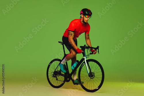 Young sportsman, cyclist on bicycle in sports uniform and protective helmet training isolated on green background. Concept of active life, rest, travel, energy, sport