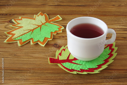 A cup of tea stands on a decorative autumn leaf. Decorative autumn leaves are made of felt. Felt cup coaster. DIY.