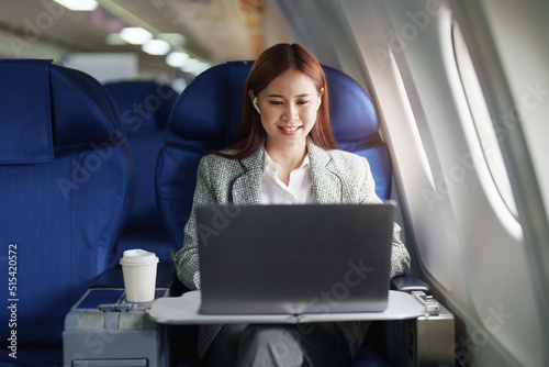 portrait of A successful asian businesswoman or female entrepreneur in formal suit in a plane sits in a business class seat and uses a computer laptop during flight © Jirapong