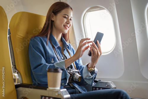 Attractive portrait of Asian woman sitting at window seat in economy class using mobile phone during plane flight, travel concept, vacation