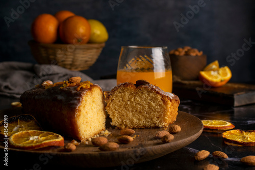 orange cake pudding with almonds and whole and sliced natural oranges and orange juice on a dark table