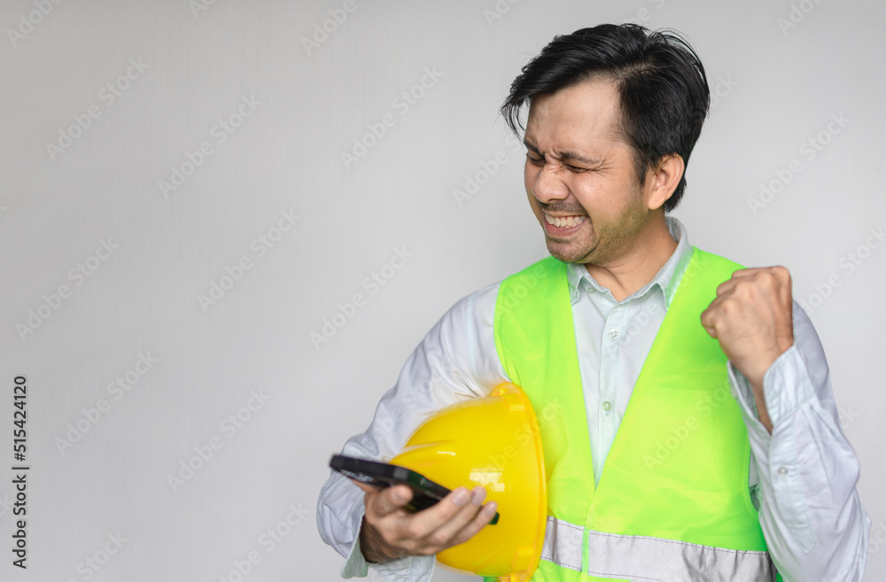 Male Asian construction worker holding smartphone and raising his hand showing success with copy space Male Asian construction worker holding smartphone and raising his hand showing success with copy space