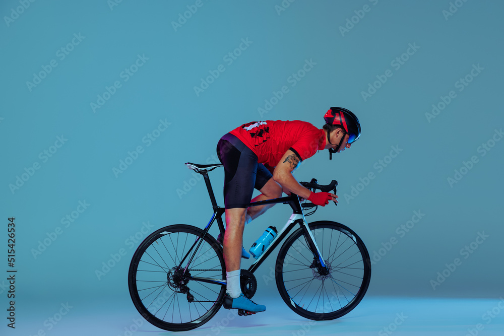 Naklejka premium Studio shot of professional cyclist in red sports uniform, goggles and a helmet on a blue background. Concept of active life, rest, travel, energy, sport