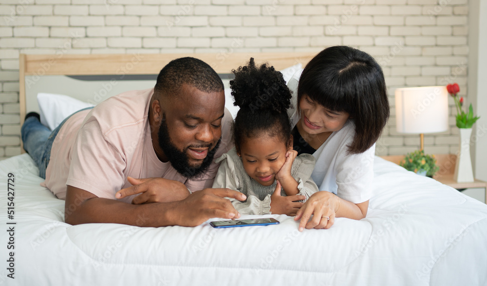 The family has fun and plays education games online with a smartphone at home in the bedroom. Concept of online education and caring from parents. The family has fun and plays education games online with a smartphone at home in the bedroom. Concept of online education and caring from parents.