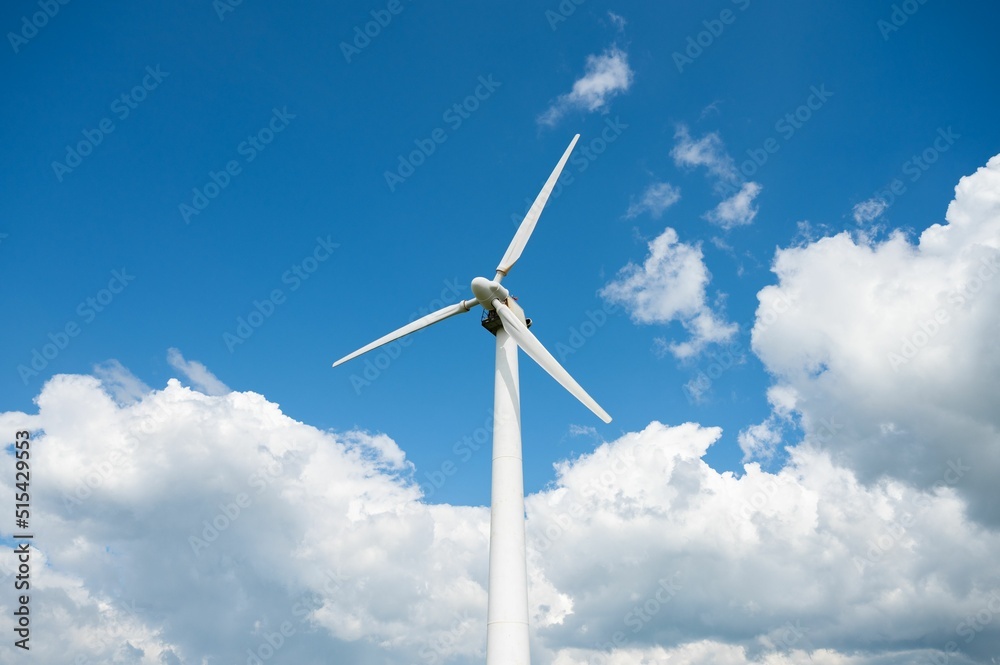 Low angle of wind turbine's giant propellers under the cloudy blue sky