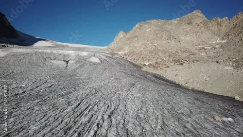 large glacier with ridges and crevasses creating a plain in swiss high rocky mountains, drone push in shot photo