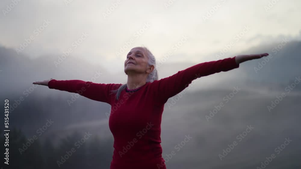 Senior woman doing breathing exercise in nature on early morning with fog and mountains in background. Senior woman doing breathing exercise in nature on early morning with fog and mountains in background.