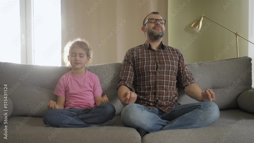 Father and Her Daughter Are Meditating Smiling While Sitting in Yoga Pose on Sofa at Home. Healthy Family Kid Girl and Father Having Fun Doing Yoga Exercises Together Sit in Lotus Pose. Relaxation Father and Her Daughter Are Meditating Smiling While Sitting in Yoga Pose on Sofa at Home. Healthy Family Kid Girl and Father Having Fun Doing Yoga Exercises Together Sit in Lotus Pose. Relaxation