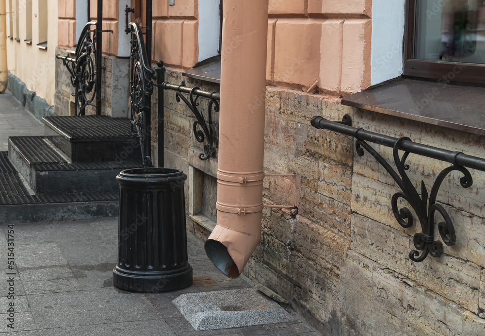 The trash can stands next to the drain pipe on the city street The trash can stands next to the drain pipe on the city street