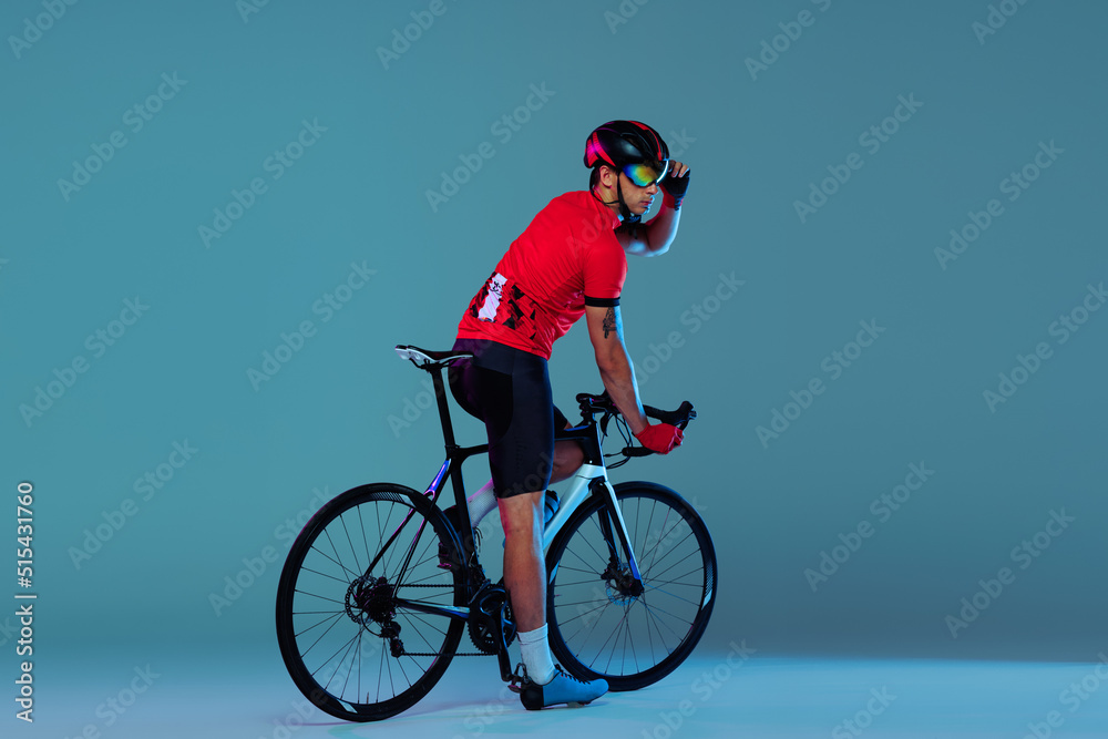 Naklejka premium Studio shot of professional cyclist in red sports uniform, goggles and a helmet on a blue background. Concept of active life, rest, travel, energy, sport