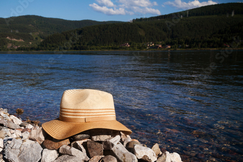 A lady's straw hat lies on the riverbank on a sunny day.