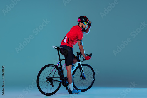 Fototapeta Naklejka Na Ścianę i Meble -  Studio shot of professional cyclist in red sports uniform, goggles and a helmet on a blue background. Concept of active life, rest, travel, energy, sport
