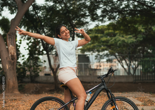 latina girl with open arms and a satisfied face riding her bicycle making the peace and love symbol with her fingers.